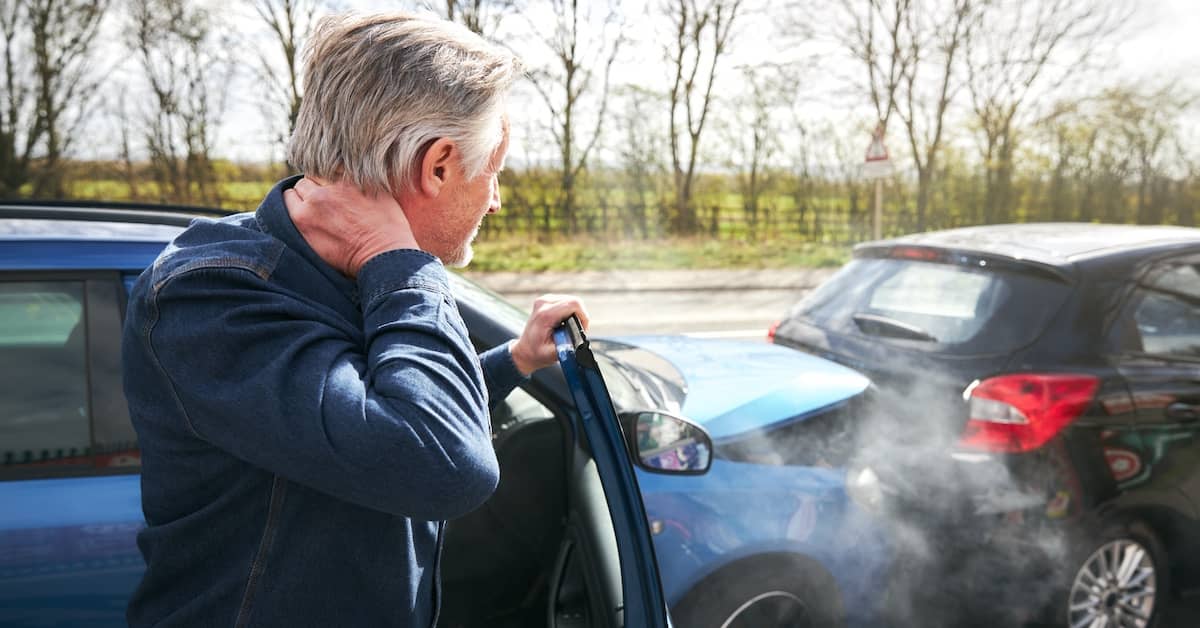 Man rubs his neck in front of car crash. | Bernheim Kelley Injury Lawyers